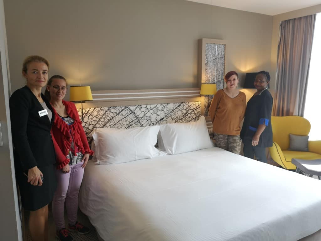 personnes accompagnées et valets de chambre devant un lit fait